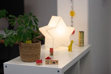 Auf einem Schränkchen stehen hölzerne, kleine Kinderspielzeuge, eine Lampe in Sternform und eine Pflanze
