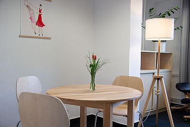 In einer Ecke des Raumes stehen ein Tisch mit Tulpenstrauß, Stühle und eine Stehlampe.