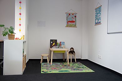 Spielecke für Kinder mit kleinem Tisch und Hockern, Büchern, Stiften und einem Plüschtier.